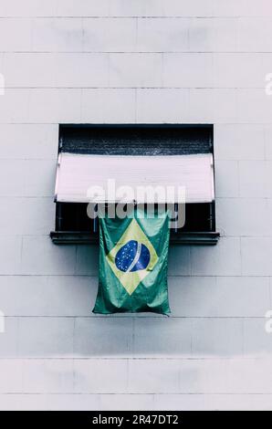 Una foto verticale della bandiera del Brasile appesa alla finestra di un muro Foto Stock