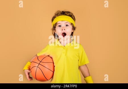 Bambino sorpreso con palla di basket. Attrezzatura sportiva. Ragazzo sportivo con basket. Sport professionale. Piccolo basketballer in abbigliamento sportivo. Sport Foto Stock