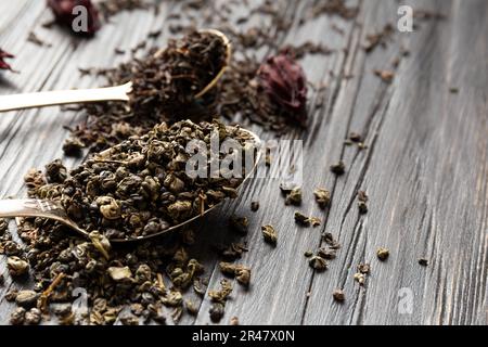 Composizione di tè nero e verde secco in cucchiai d'annata e fiori di ibisco secco su uno sfondo di legno scuro primo piano. Diversi tipi di tè secco Foto Stock
