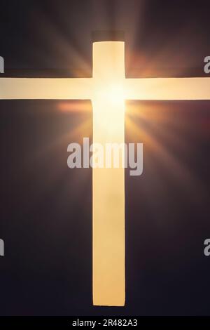 Una croce cristiana illuminata da un raggio di sole su sfondo nero Foto Stock