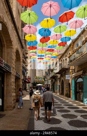 I pedoni camminano sotto ombrelli colorati sospesi sopra la via Yoel Solomon a Nahalat Shiva, il terzo quartiere costruito fuori dalla città Vecchia di Gerusalemme negli anni '1860 Oggi è un affollato viale pedonale fiancheggiato da caffetterie sul marciapiede. Gerusalemme Ovest Israele Foto Stock