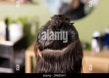 Vista posteriore della cliente caucasica con capelli bagnati agganciati sulla testa di fronte allo specchio del salone dei capelli Foto Stock