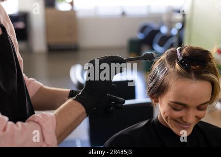 Sezione centrale del parrucchiere caucasico maschio in guanti tintura capelli di felice cliente femminile al salone Foto Stock