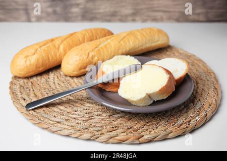 Baguette intere e tagliate con burro fresco su tavola bianca Foto Stock