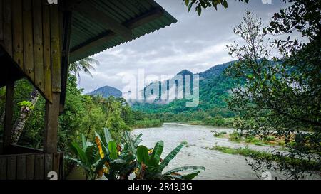 Una tranquilla cabina si trova in una tranquilla zona boschiva accanto ad un lago con montagne sullo sfondo Foto Stock