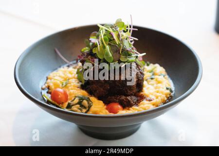 Una ciotola di ceramica nera riempita con un piatto di risotto cremoso, sormontata da una fetta di bistecca di manzo Foto Stock