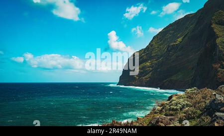 Una spiaggia rocciosa con un mazzo d'acqua in essa con alberi verdi sulla collina, Madeira, Portogallo Foto Stock