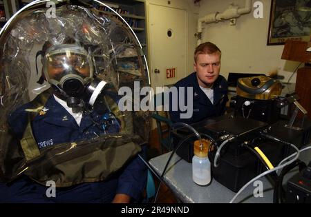 US Navy Fire Controlman classe 1st ha un test di adattamento eseguito sulla sua maschera di gas MCU-2-P, mentre Damage Controlman classe 3rd monitora le letture Foto Stock