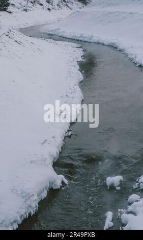 Un ruscello tranquillo si snoda attraverso un paesaggio invernale incontaminato di campi innevati Foto Stock