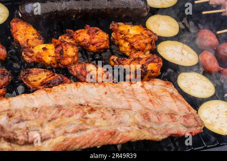 Una gamma di deliziose carni e verdure cucinate su una griglia esterna Foto Stock