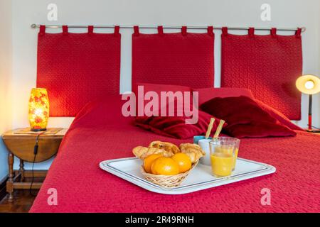 Un vassoio bianco con succo d'arancia appena spremuto e biscotti per la colazione in una stanza sul letto Foto Stock