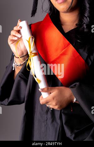 Una giovane laureata che si è orgogliosamente laureata in regalia accademica con il suo diploma Foto Stock