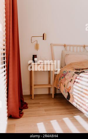 Camera da letto moderna con letto e comodino, situata di fronte alle tende rosse Foto Stock