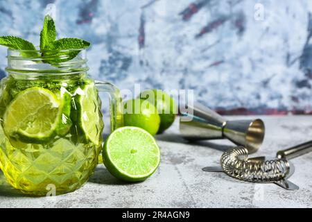 Barattolo Mason di mojito freddo e shaker con lime su tavolo blu Foto Stock