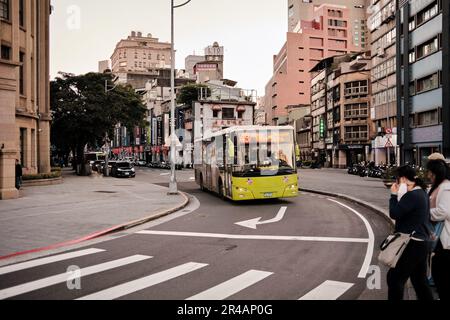 Un gruppo diversificato di pedoni in attesa di attraversare una strada urbana trafficata come un grande autobus pubblico in auto vicino in background Foto Stock