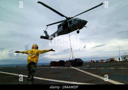 US Navy Un segnale di atterraggio arruolato Sailor guida un MH-60s Seahawk elicottero, assegnato a Helicopter Combat Support Squadron Five (HC-5), durante un rifornimento verticale a bordo del comando militare Sealift (. Foto Stock