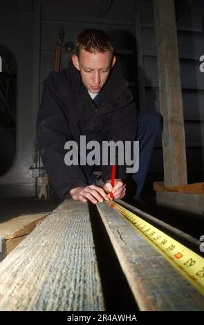 US Navy Damage Controlman 3rd Classe misura il legno prima di tagliarlo. Foto Stock