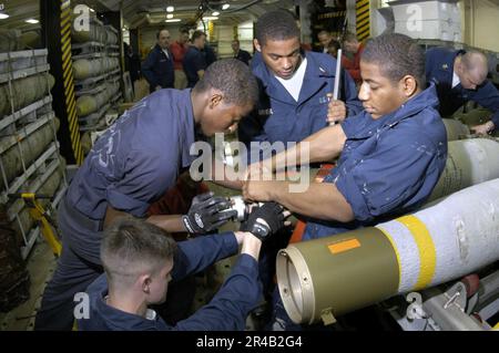 I marinai della Marina STATUNITENSE assegnati al Dipartimento delle armi trasportano uno skid di armi caricato con tre bombe di uso generale da 83 1.000 libbre nella baia dell'hangar a bordo della portaerei a propulsione convenzionale USS Ki. Foto Stock