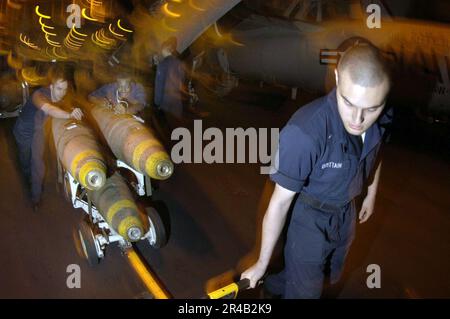 I marinai della Marina STATUNITENSE assegnati al Dipartimento delle armi trasportano uno skid di armi caricato con tre bombe di uso generale da 83 1.000 libbre nella baia dell'hangar a bordo della portaerei a propulsione convenzionale USS Ki. Foto Stock