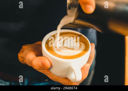 Il latte schiumato viene versato nel cuore di una tazza di caffè Foto Stock