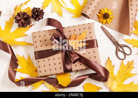 Confezione regalo. Scatola regalo di carta fatta a mano con foglie essiccate, coni di pino su bianco. Regalo di festa creativa autunnale. Giorno di ringraziamento, caduta backgro Foto Stock