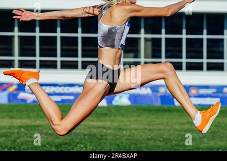 primo piano atleta femminile salto triplo nei campionati estivi di atletica sul campo verde sfondo Foto Stock