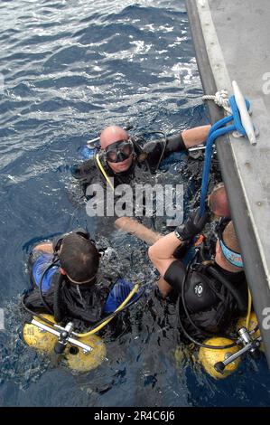 US Navy Mobile Diving and Salvage Unit One distaccamento tre membri sono in piedi in superficie mentre aspettano il resto della loro squadra di entrare in acqua. Foto Stock