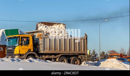 Dicembre 23, 2021. Regione di Kemerovo, Russia. Il trattore arancione grande pulisce la neve dalla strada e la carica nel carrello. Pulizia e pulizia della strada Foto Stock