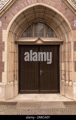 Una foto verticale di due porte in legno affiancate su un edificio in mattoni adornato da una croce Foto Stock