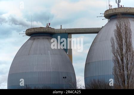 Una scena industriale rustica caratterizzata da due alti barili di metallo con un ponte di legno intemperiato sopra di loro, adagiato contro un cielo blu chiaro Foto Stock