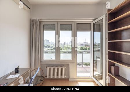 Grande finestra di una camera con una porta d'uscita su una terrazza con vista su un parco urbano Foto Stock