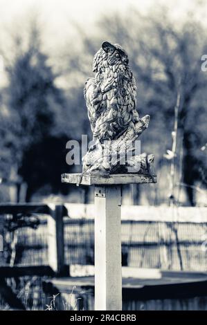 Una statuetta riccamente ornata è appollaiata in cima a un palo di recinzione di legno circondato da un lussureggiante e verde fogliame Foto Stock