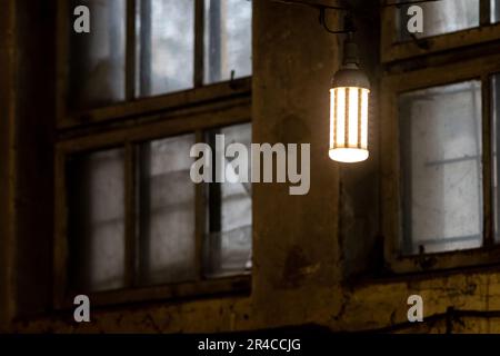 Una lampada a sospensione bianca in stile retrò è sospesa ai lati di un edificio in mattoni, illuminata dalla luce del sole che scorre attraverso il vicino vetro della finestra Foto Stock