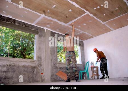 US Navy Builder Constructionman Apprentice assegnato a Naval Mobile Construction Battalion One (NMCB-1) lavora con un Navy Seabee Filippino per preparare un soffitto in compensato per la vernice. Foto Stock