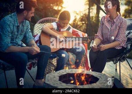 Una madre, un padre e una figlia si riunirono intorno ad un caminetto accogliente, indulgendo nella deliziosa attività di arrostire marshmallows. Nel frattempo, il loro talento d Foto Stock