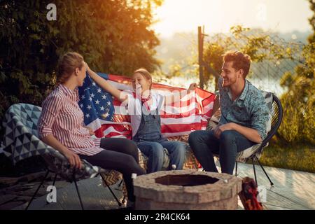 Una famiglia gioiosa che celebra l'Independence Day all'aperto. L'immagine presenta una madre, un padre e una figlia seduti intorno a un accogliente fossa del fuoco, il loro volto è Foto Stock