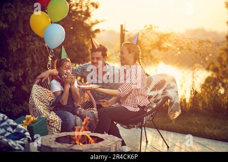 La madre tiene in mano una torta di compleanno, mentre il volto della figlia è giocosamente coperto di panna montata mentre scoppia in risate. Le espressioni sul thei Foto Stock