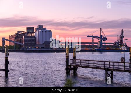 Molo commerciale con silos e vecchie warwhouses su un porto fluviale al crepuscolo Foto Stock