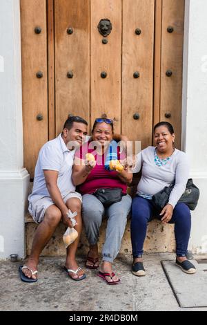 Un uomo e due donne sorridono mentre si siedono davanti a una porta di legno in una strada nella Città Vecchia di Cartagena Colombia Foto Stock