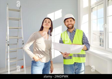 Giovane padrona di casa donna in piedi con un caposquadra nel suo nuovo appartamento vuoto e sorridente. Foto Stock