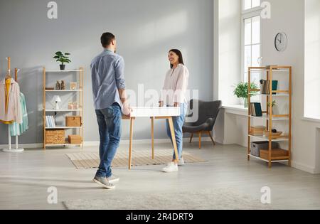 Felice giovane marito e moglie spostare mobili e portare un nuovo tavolo insieme Foto Stock