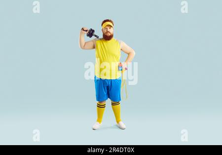 Divertente serio atleta maschile grasso con attrezzature sportive su sfondo pastello azzurro. Foto Stock