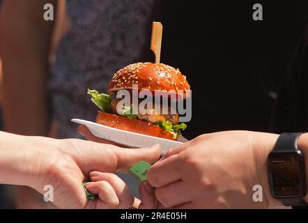 Vendita di hamburger in un mercato agricolo di strada. Il cliente consegna all'addetto una polizza di pagamento e prende l'hamburger da lei su un vassoio di carta Foto Stock