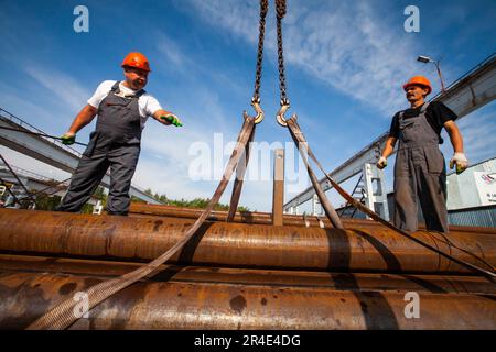 Podolsk, provincia di Mosca - 02 agosto 2021: Deposito tubi. Gli operatori montano le cinghie per il sollevamento Foto Stock