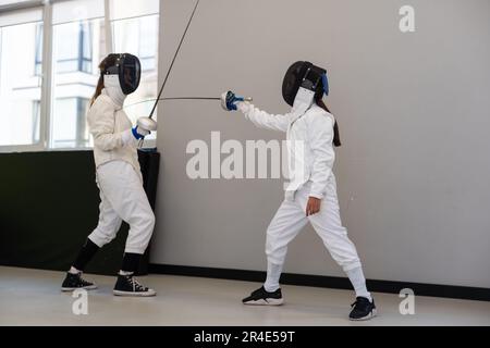 Due atleti di scherma lottano in un'arena sportiva professionale Foto Stock