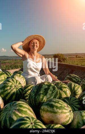 donna anguria. Si siede in un cappello su una montagna di cocomeri. Rimorchio con cocomeri nel mercato. Foto Stock