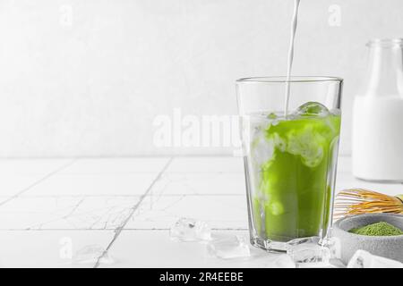 Versare il latte o la crema in un bicchiere di latte verde opaco ghiacciato su fondo bianco. Bevanda estiva fredda Foto Stock