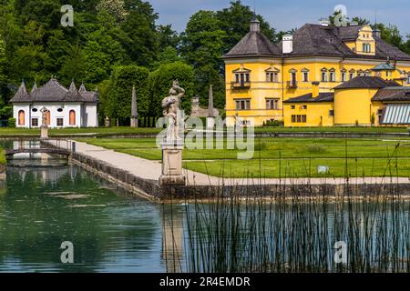 Il palazzo di Hellbrunn si riflette nel parterre d'acqua del suo parco a Salisburgo, in Austria. Un padiglione bianco e diverse figure di pietra costeggiano lo stagno ornamentale. Foto Stock