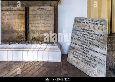 Una targa commemorativa per Monsignor Franz Sr. Anthaller (1821–1903), camerlengo papale e presidente diocesano di diverse associazioni cattoliche, è appoggiata contro un muro del Cimitero di San Sebastiano a Salisburgo, Austria, accanto a antiche iscrizioni tombali erose. Foto Stock