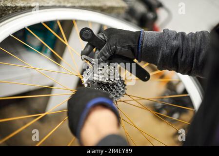 Manutenzione di una bicicletta: Mani di una persona non riconoscibile utilizzando guanti smontando il set di pignoni di una ruota per bicicletta presso il suo negozio di riparazione. Foto Stock